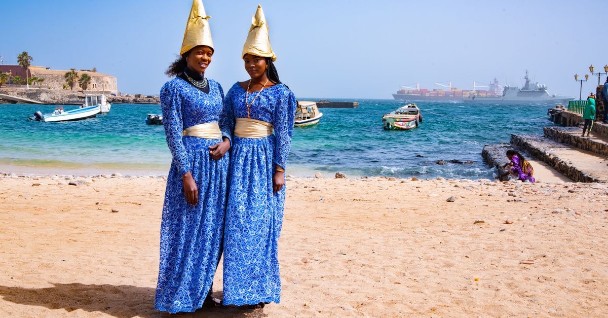 Dakar travel guide: West Africa's coastal capital Two women in blue traditional dresses with cone hats on a sunny beach in Dakar, Senegal.