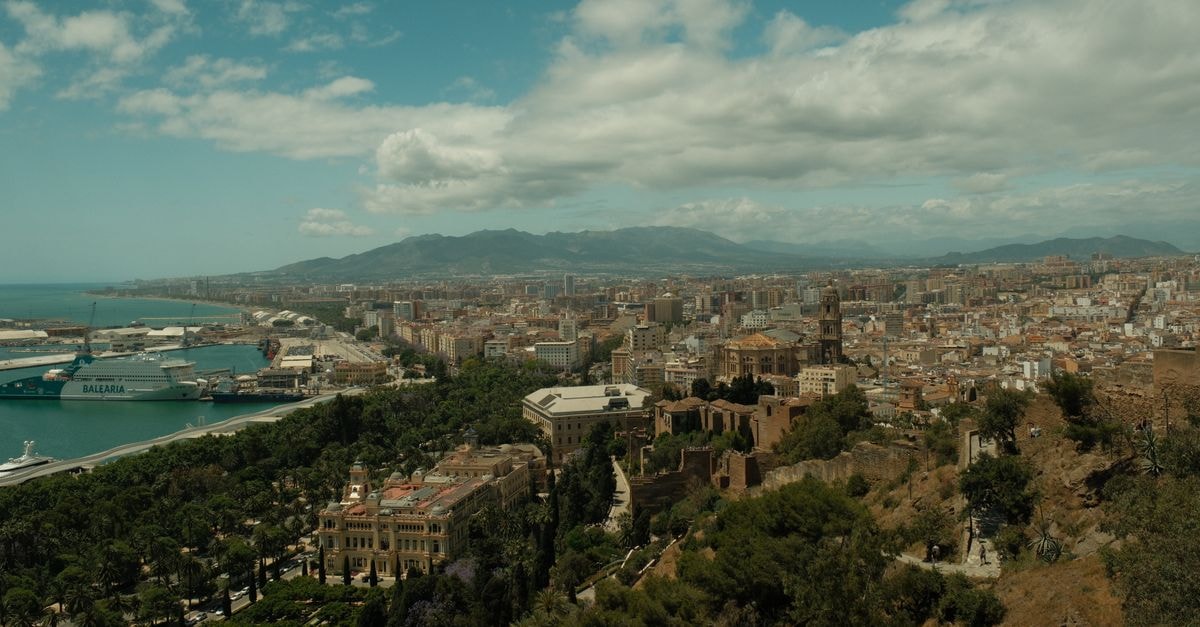 Aerial view of Malaga city, showcasing the harbor and cityscape under a cloudy sky.