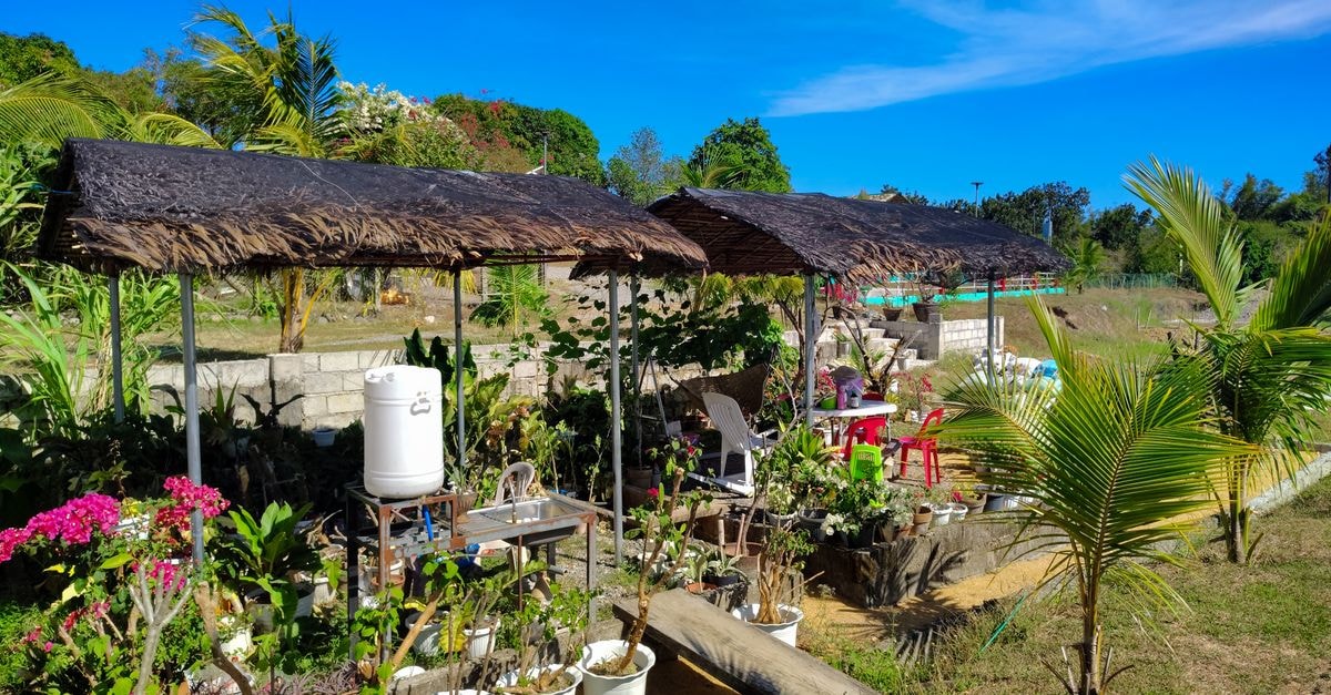Slow Days in Malingao: A Quiet Soccsksargen Travel Guide A serene tropical garden setting in the Philippines with thatched huts and lush green plants under a vibrant blue sky.