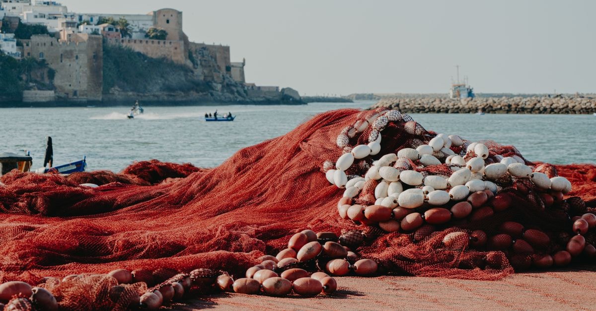 Kenitra Travel Guide: Practical Tips for a Coastal Moroccan City Vibrant fishing nets on the shore with a historical fortress in Rabat, Morocco, a blend of tradition and scenery.