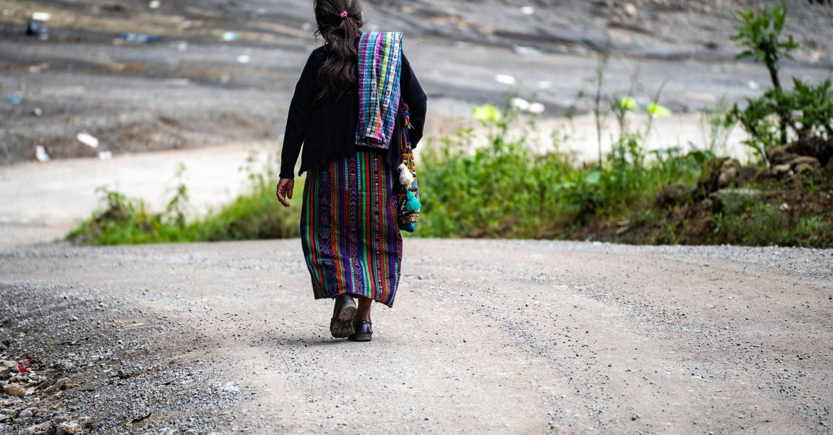 A Slow Travel Guide to Totonicapán, Guatemala A woman in traditional Guatemalan attire walks on a rural path, showcasing cultural and natural beauty.