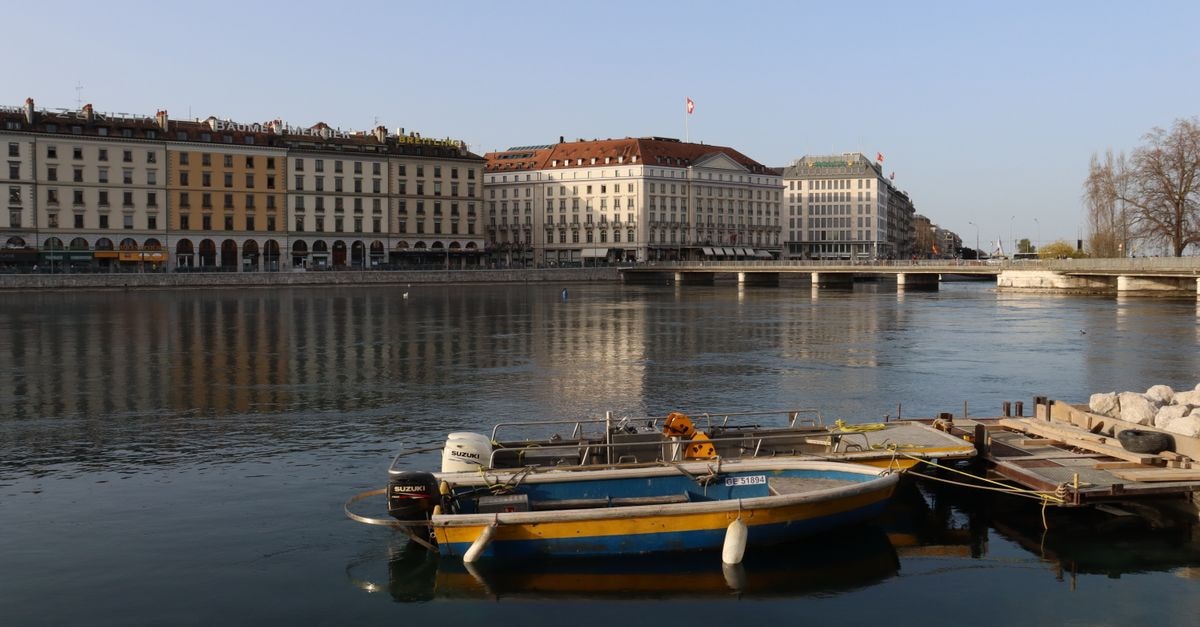 Scenic view of boats docked by the Geneva waterfront with historic buildings reflected on the calm water.