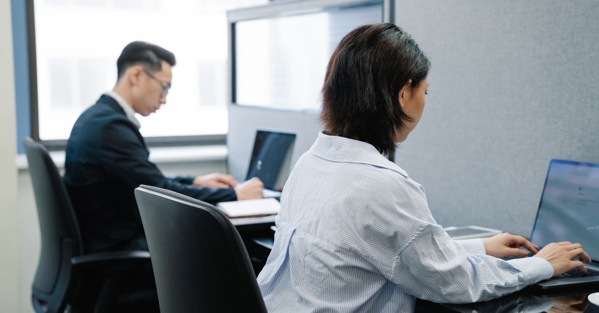 Two professionals working on laptops in a modern office cubicle setup.