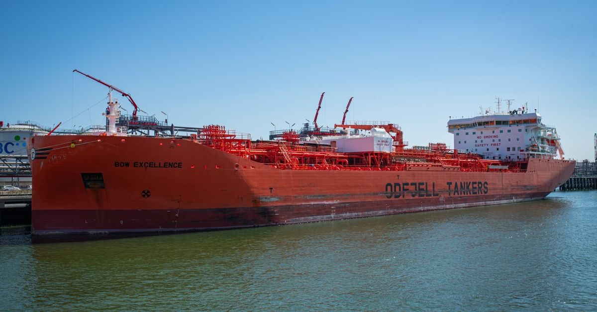 A large red oil tanker named Bow Excellence docked at a harbor under clear blue skies.