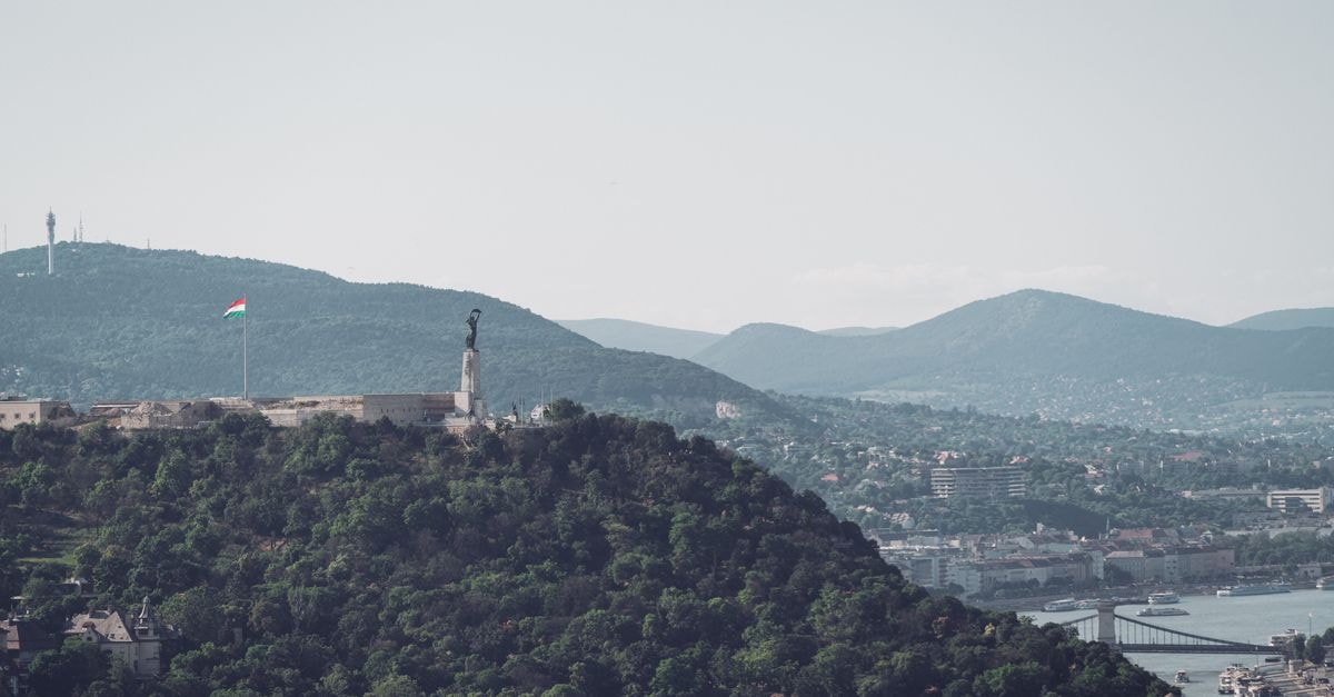Scenic view of Budapest featuring the iconic Liberty Statue and lush hills under a clear sky.