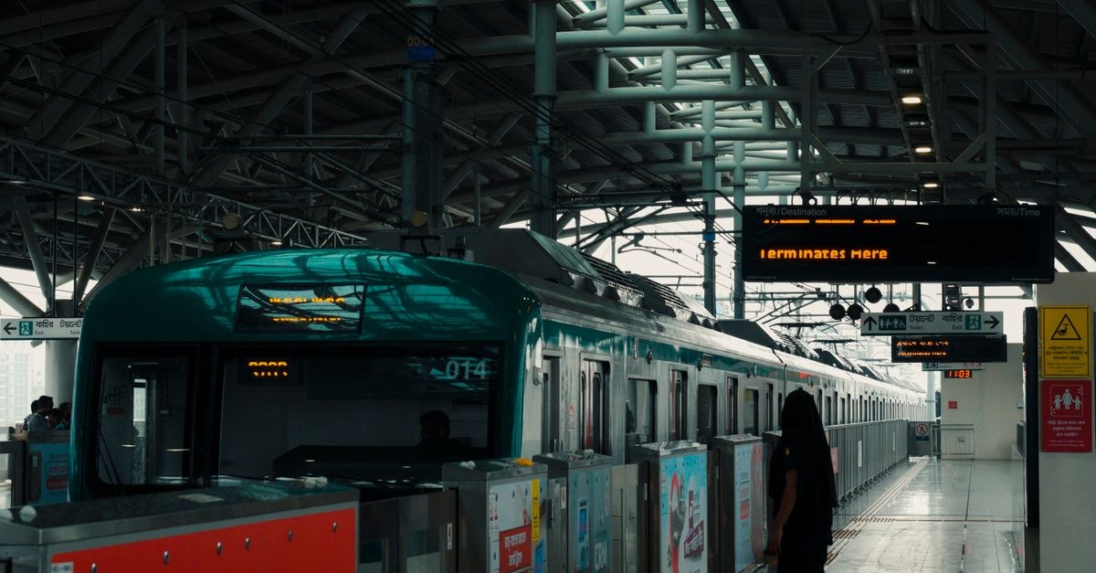 A modern metro train arrives at a busy urban station platform under a large metal structure.