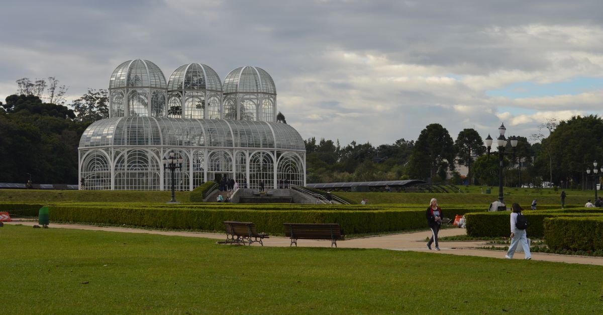 Scenic view of the Botanical Garden in Curitiba, featuring the iconic glass greenhouse under a cloudy sky.