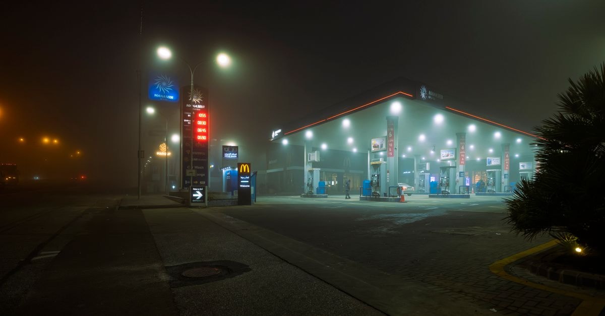 Oil Prices Slip After Iran-Driven Spike as Saudi GDP Posts Sharpest Contraction Since Pandemic A foggy night view of a well-lit gas station in Jordan, providing an atmospheric urban scene.