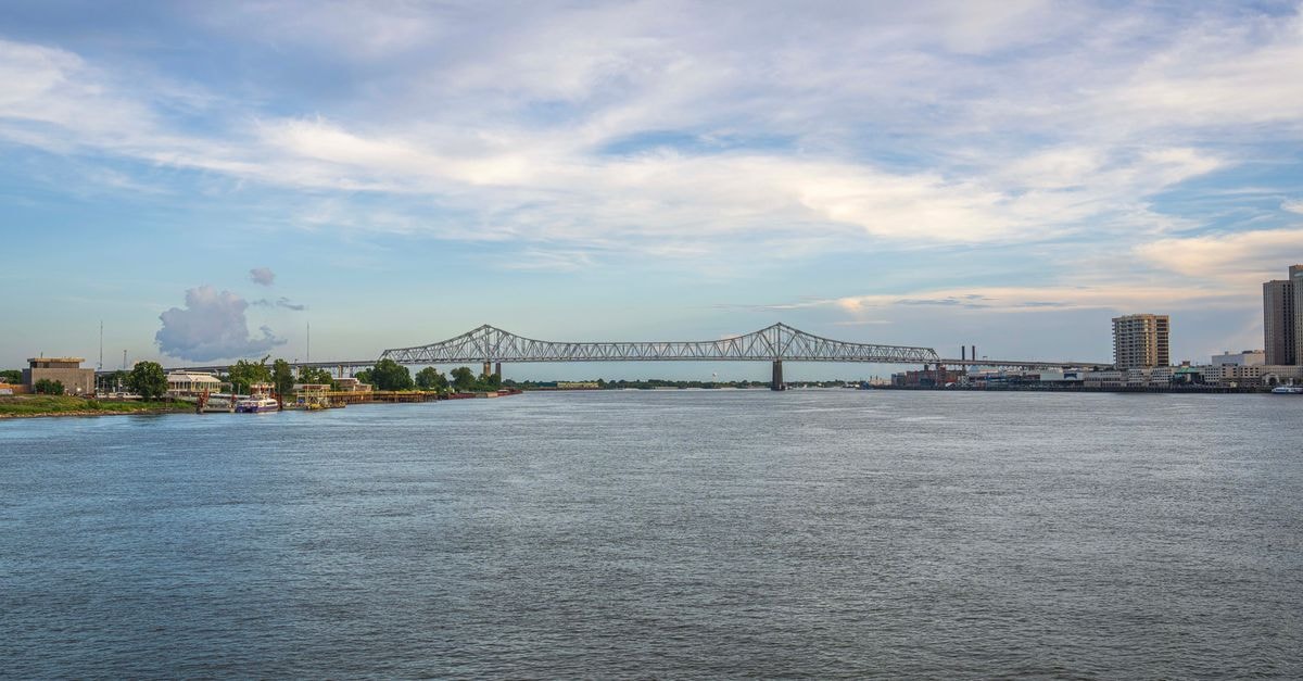 Baton Rouge Travel Guide: Planning Tips, Costs and Things to Do Calm view of bridge over Mississippi River with cityscape and blue sky in the background.