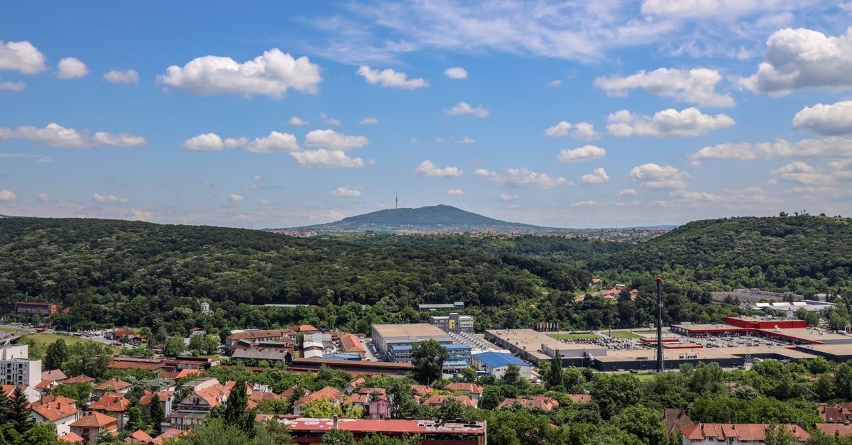 Tatabánya Travel Guide: Mining Heritage, Wine Roots, and Hilltop Views A stunning birds-eye view of a green valley with a town nestled among hills and forests.