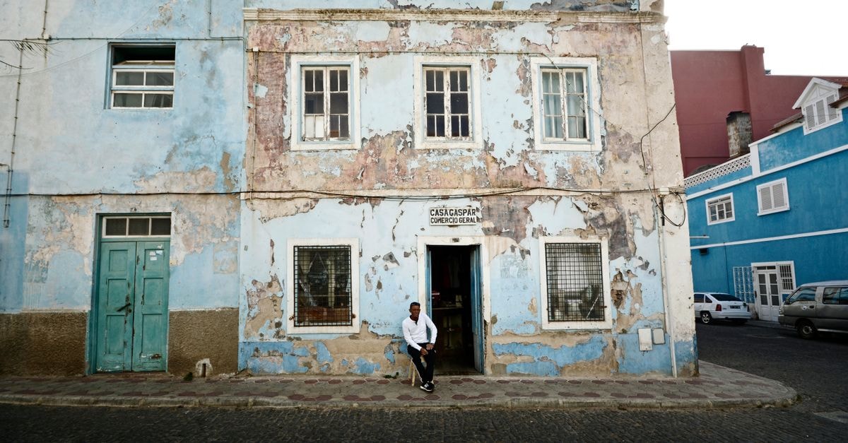 Casamarel in Mindelo: A Restored 1910 House Overlooking Mindelo Bay A weathered building with a man sitting outside in the urban streets of Mindelo, Cape Verde.