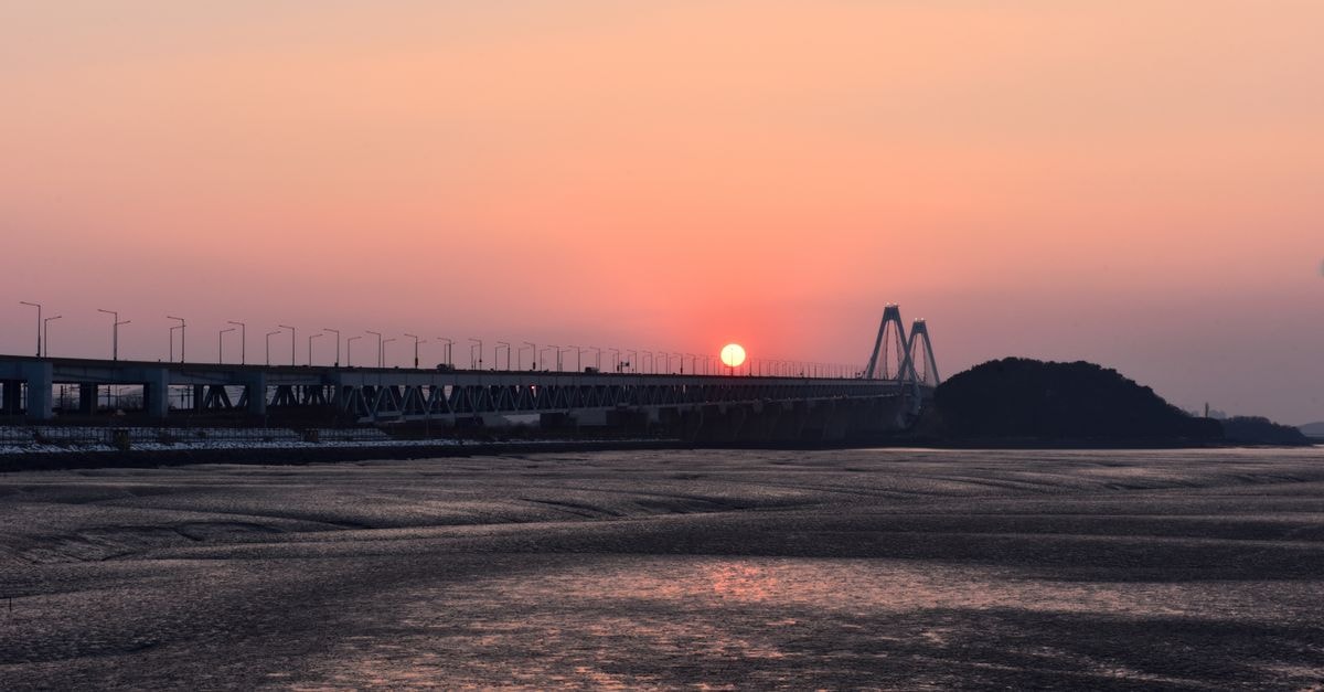 Captivating view of Yeongjong Bridge during sunset in Incheon, South Korea with serene waters and a warm orange sky.
