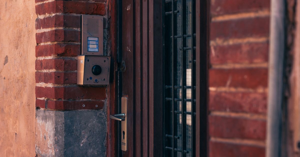 Close-up of a brick wall with a security intercom and door handles in Toulouse, France.