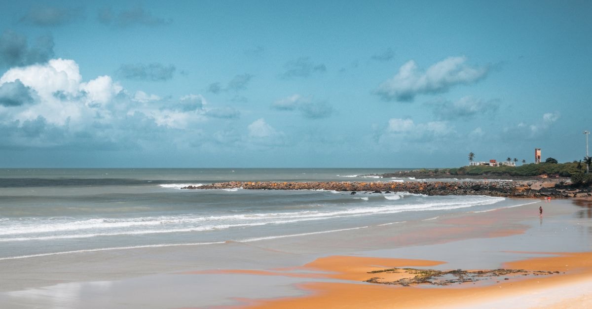 Tranquil view of a scenic beach in Natal, Brazil showing waves and a distant lighthouse.