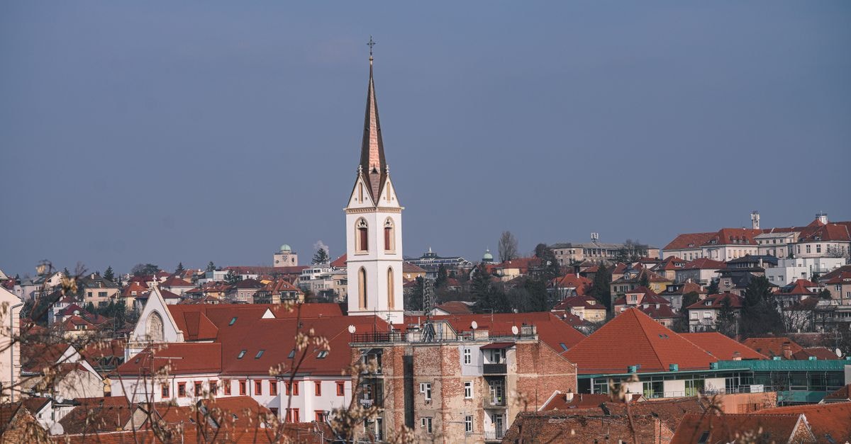 Picturesque European townscape featuring red rooftops and a prominent church spire under a clear sky.
