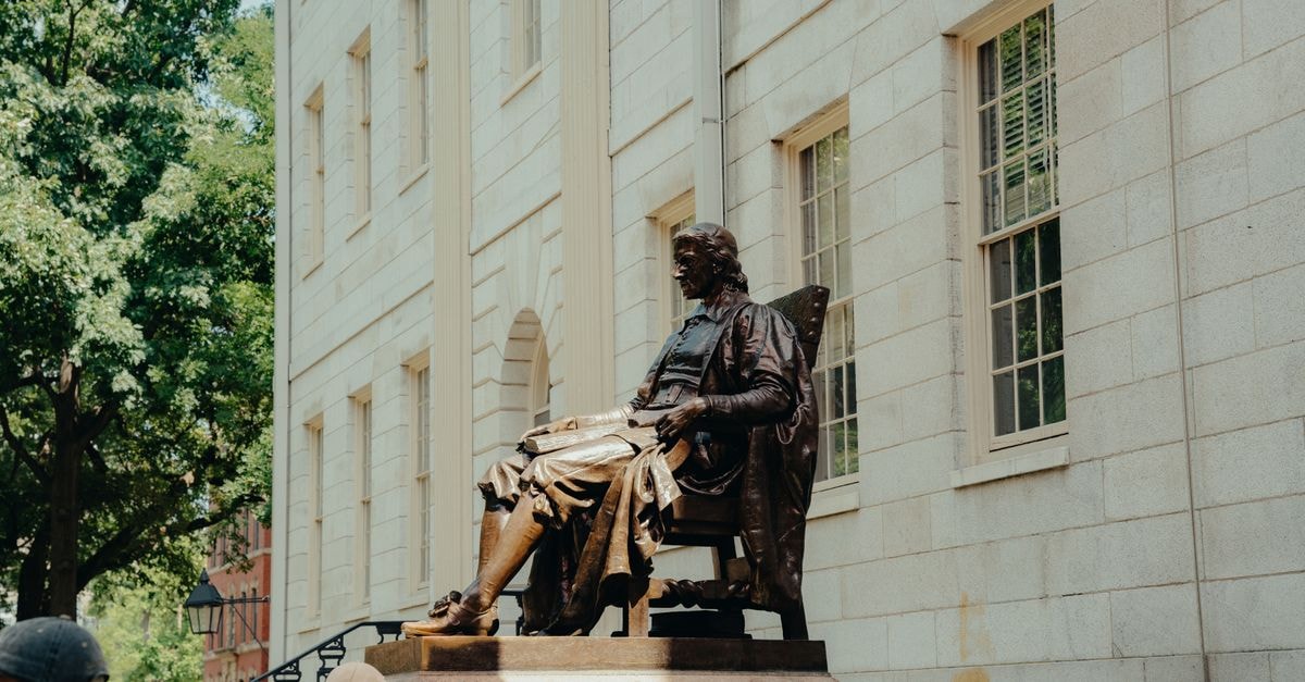 University Arms in Cambridge: Edwardian Elegance on Parker's Piece Bronze statue of a historical figure with tourists at Harvard, captured on a bright summer day.