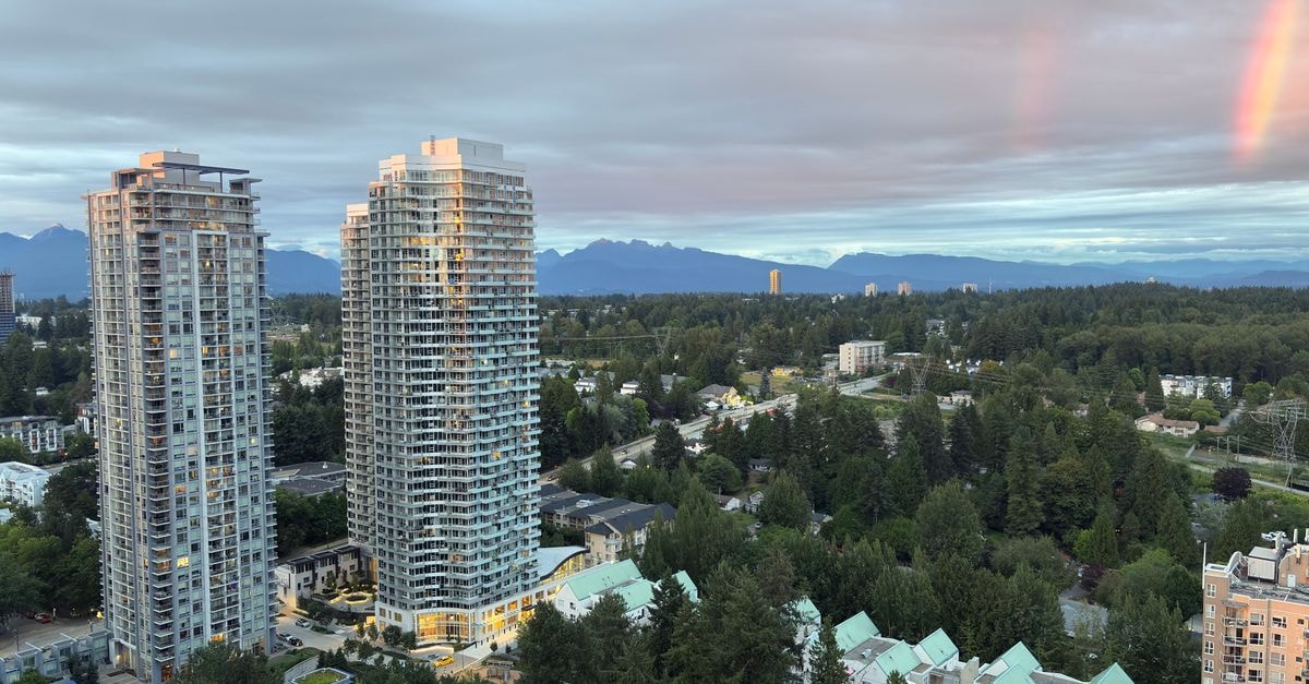 Scenic aerial view of Surrey's high-rise buildings with mountains and rainbow during sunset in British Columbia, Canada.