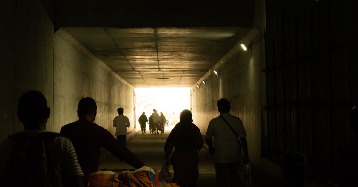 Silhouetted people walking through a tunnel leading to a bright exit in Tamil Nadu, India.