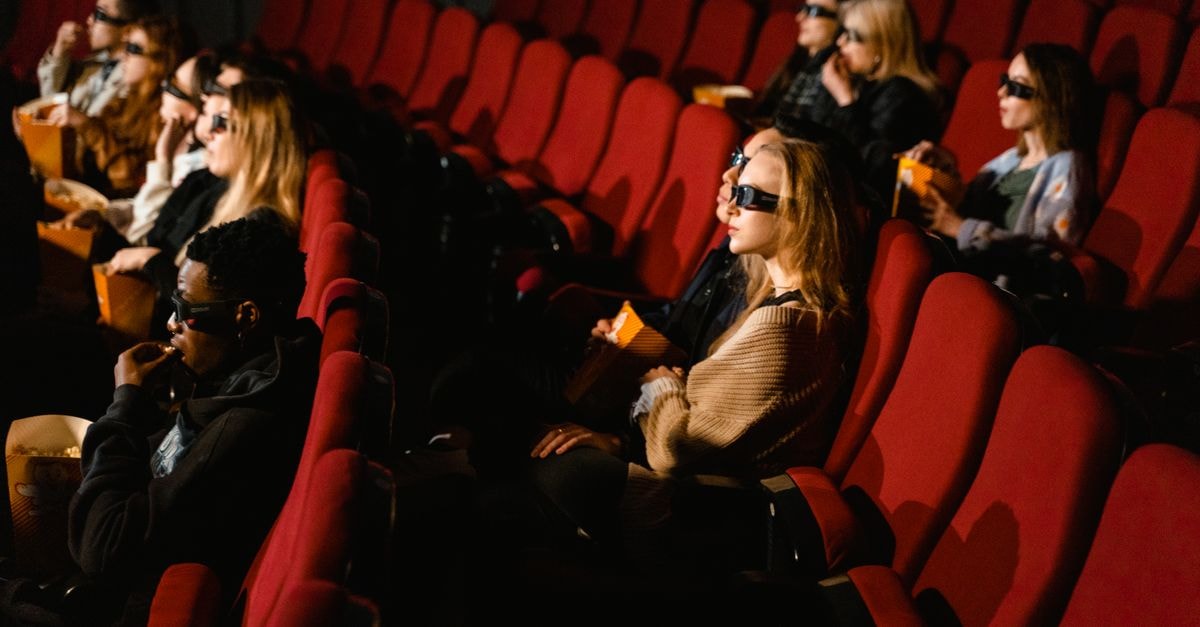 Tamil film producers halt new releases from September 1 over eight-week OTT window dispute People wearing 3D glasses and eating popcorn in a cinema with red chairs.
