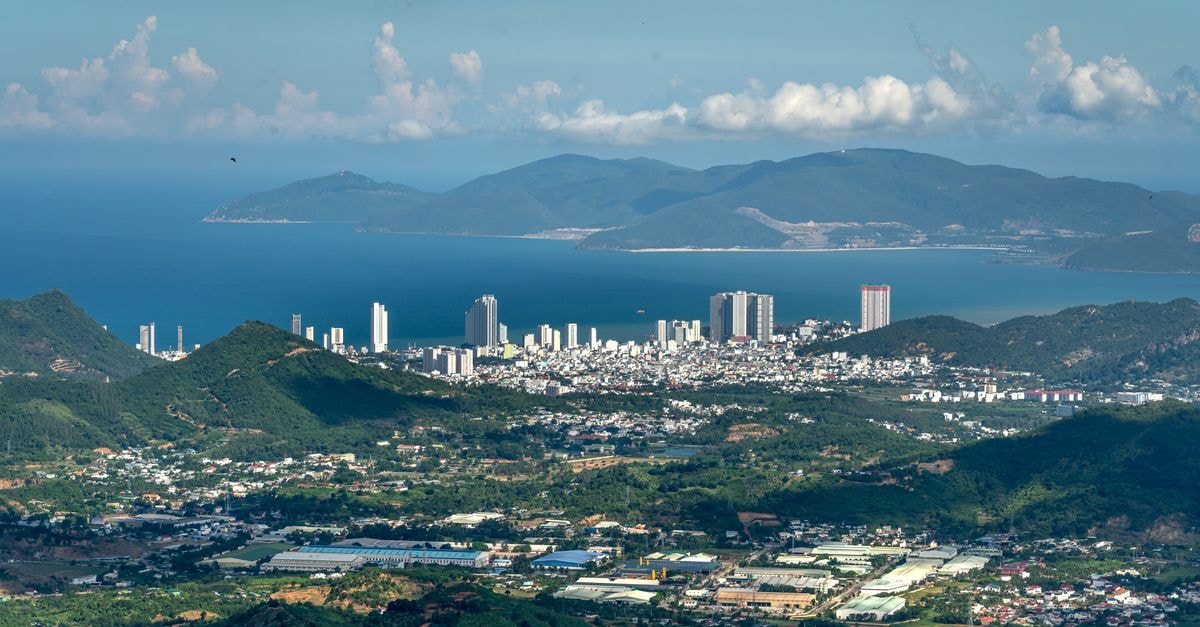 Dynamic aerial shot of a coastal city surrounded by mountains and sea under a bright sky.