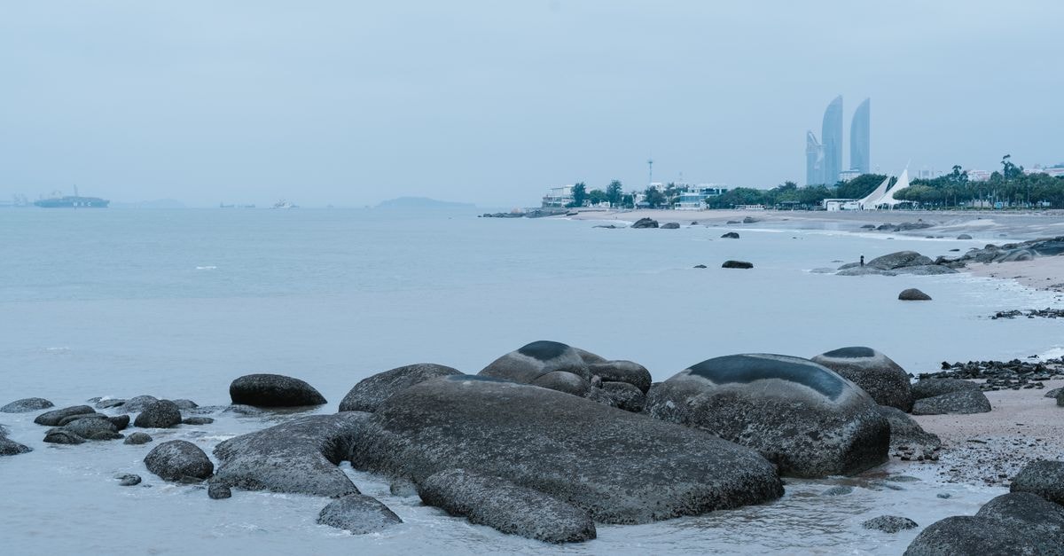 Things to Do in Zhanjiang: A Quiet Coastal City Worth Exploring Rocky shoreline with cityscape in the background and calm ocean waves.