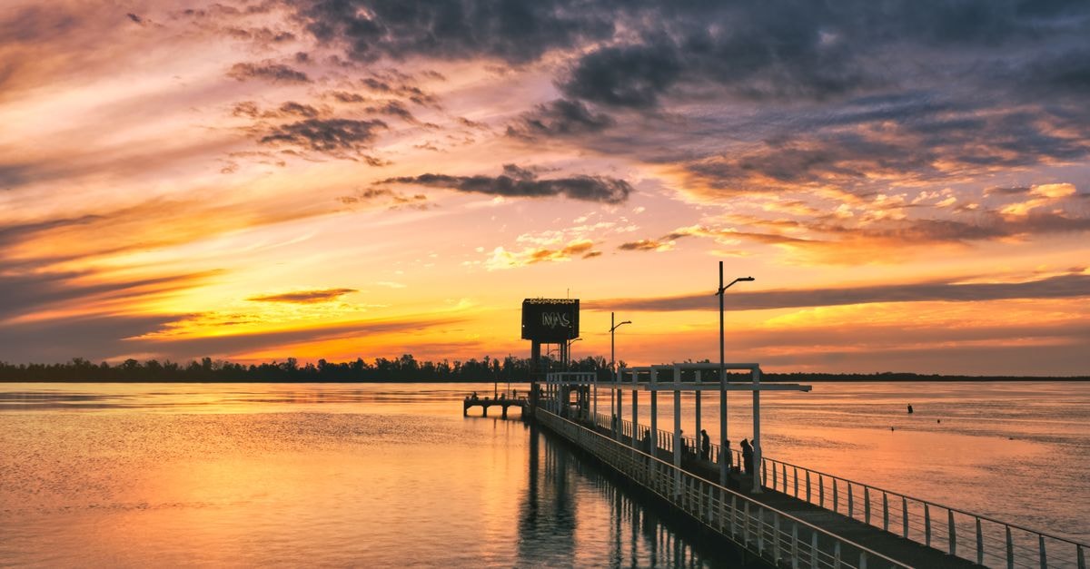 Hotel Bulevar in Paysandú: Classic Stay on Bulevar Artigas Beautiful sunset reflecting over the water at Paysandú pier, with a vibrant orange sky and clouds.
