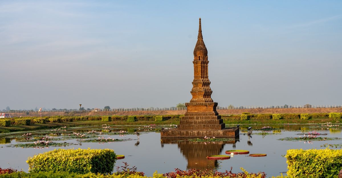 Tranquil scenery featuring a historic tower reflecting in a pond surrounded by greenery.