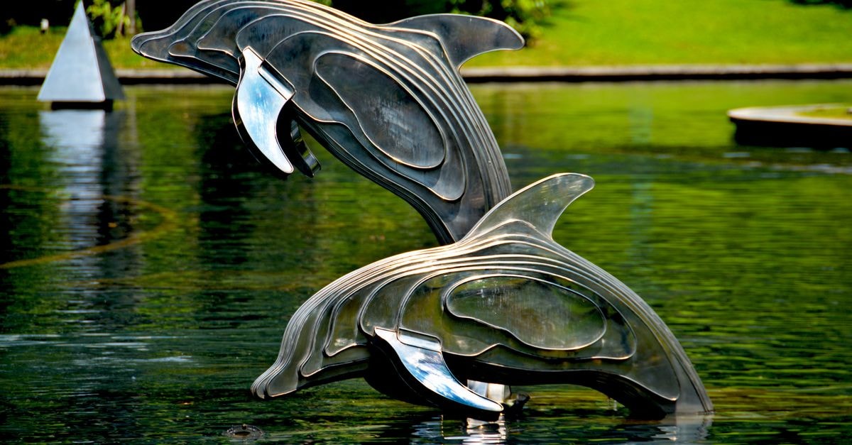 Dolphin Hotel, Visakhapatnam — A City Centre Stay Since 1980 Stainless steel dolphin statues jump gracefully in a serene park pond, surrounded by greenery.