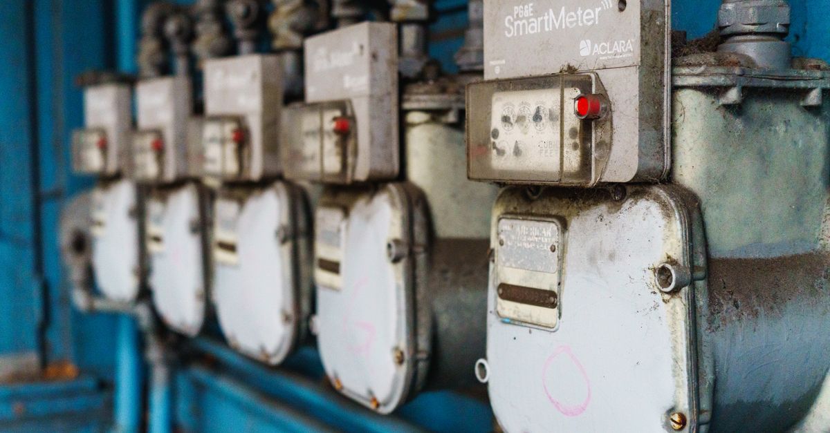 Multiple smart utility meters lined up on a blue industrial wall.