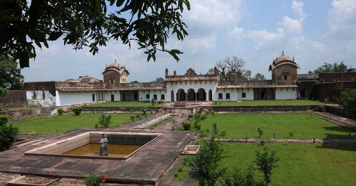 Visiting Jhansi: A Quiet Travel Guide to Bundelkhand's Storied City A historic palace courtyard with vibrant green gardens and architecture under a clear blue sky.