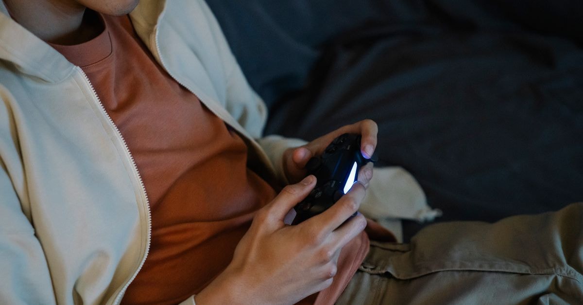 Crop anonymous man with console controller playing video game while sitting on couch in house