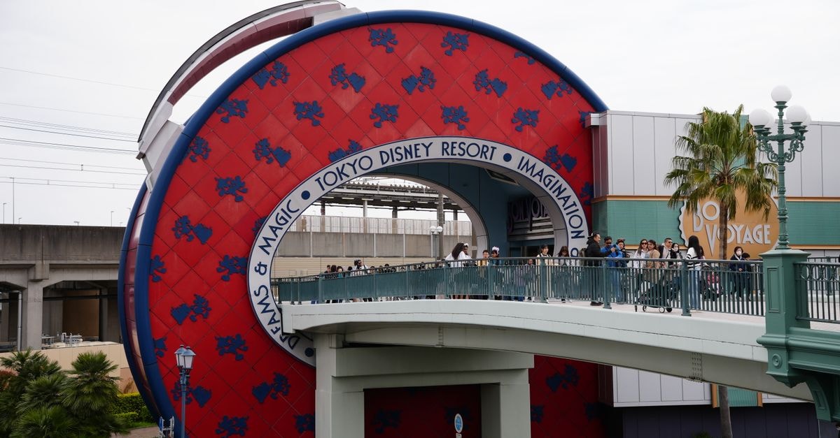 Capture of the Tokyo Disney Resort entrance featuring the Bon Voyage Store and pedestrian bridge.