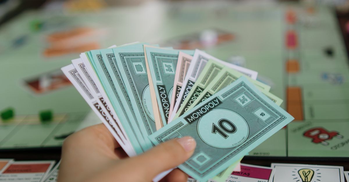 ITAT Bangalore Rules Only Net Profits From Online Real-Money Gaming Are Taxable Close-up of a hand holding Monopoly money with board game in the background.