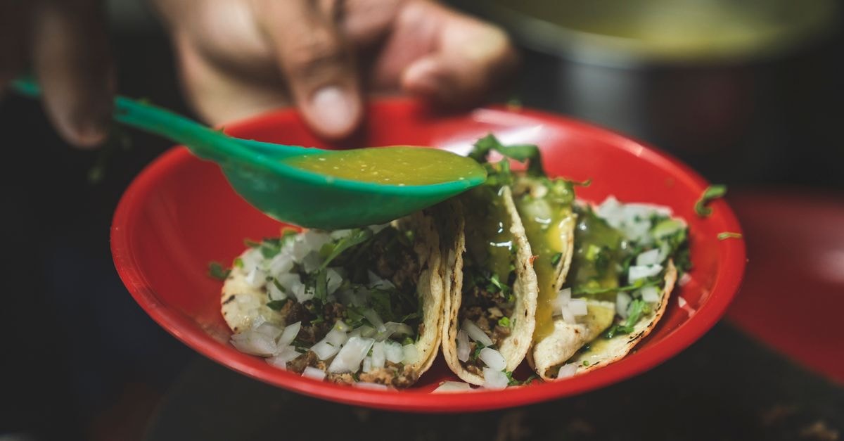 Close-up of delicious Mexican tacos being seasoned with green salsa.