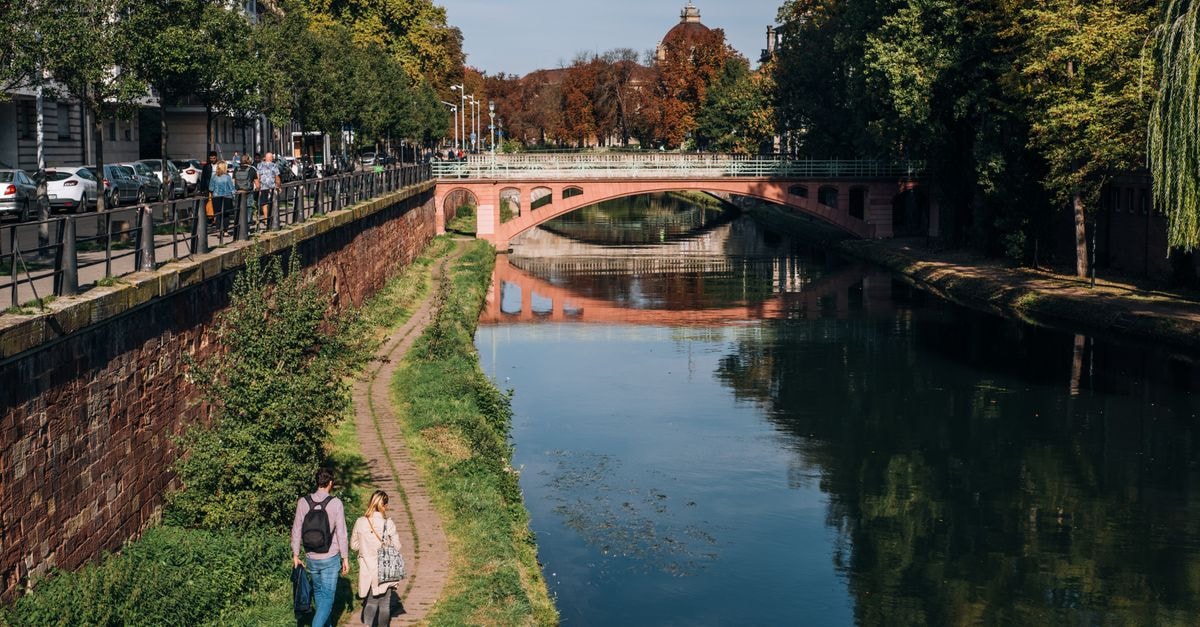 Strasbourg Travel Guide: Planning Tips, Costs and Things to Do Wide calm river under stone bridge near green park and walkway in modern city