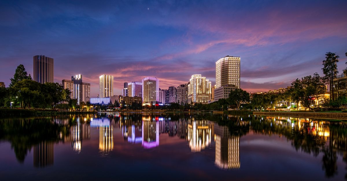 Vibrant city skyline with modern architecture reflected in a serene lake during twilight.