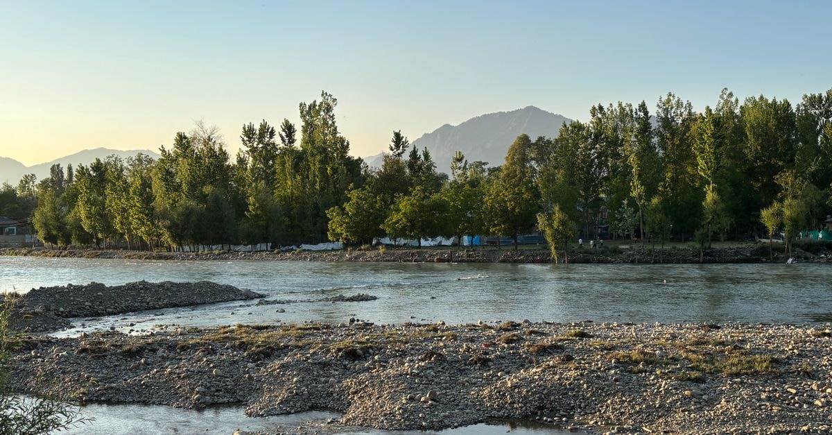 Slow mornings by the river: a Muzaffarabad travel guide Peaceful riverside landscape with lush trees and distant mountains under a clear sky at dusk.