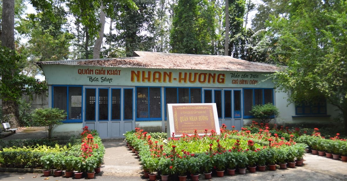 A quaint Vietnamese cafe surrounded by vibrant red flowers, offering a serene outdoor setting.
