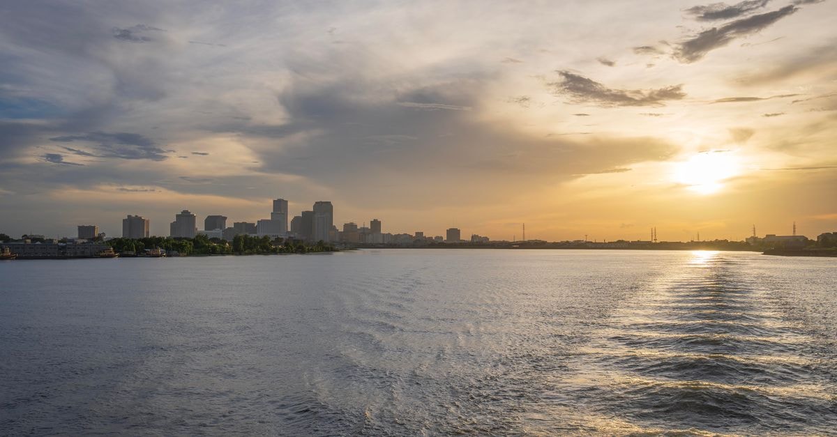 Nola Hotel in Nola, Central African Republic: A Sangha‑Mbaéré Capital Stay A serene sunset view over a city's skyline and river, casting warm light.
