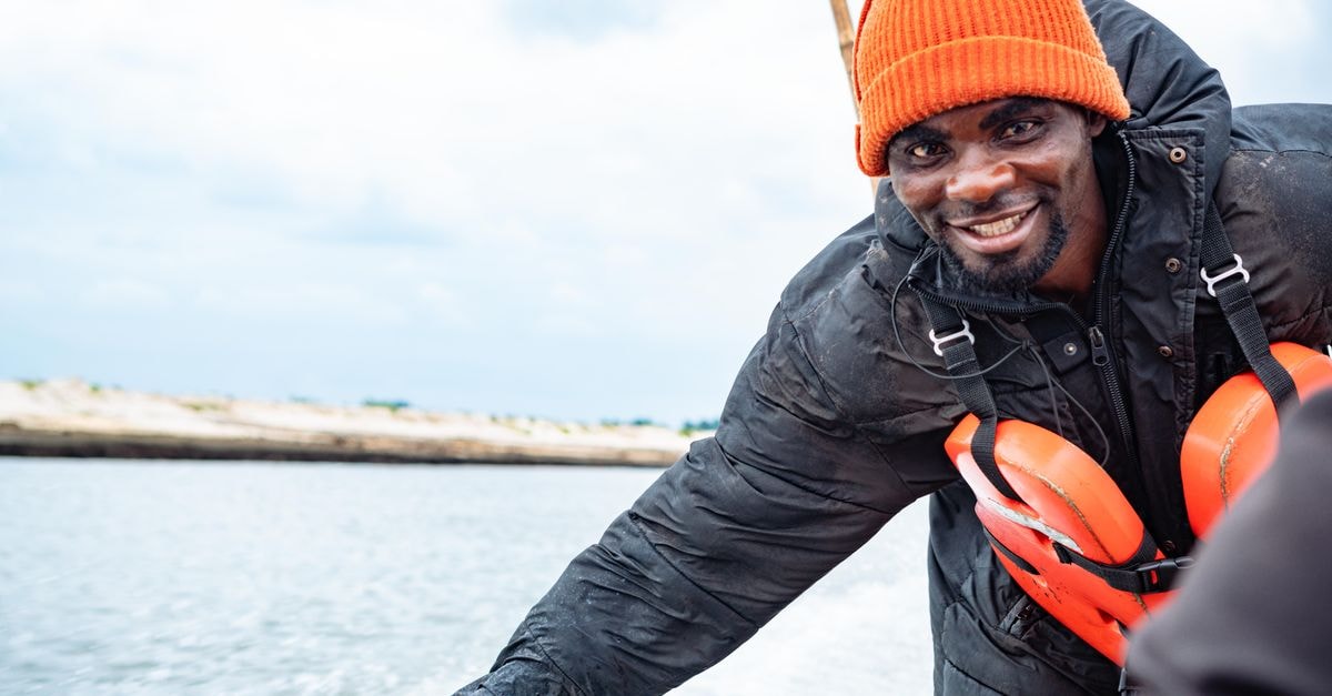 Smiling man wearing an orange hat and life jacket on a boat in Port Harcourt, Nigeria.