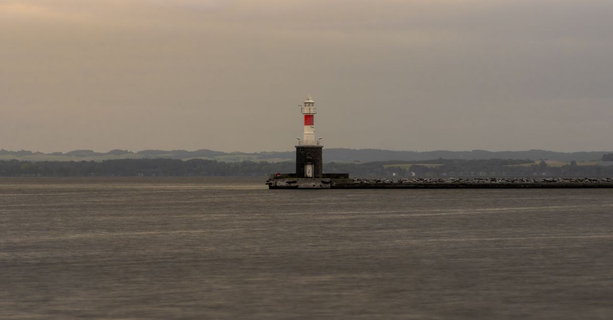 Peaceful view of a lighthouse on a breakwater during a calm evening at sea.