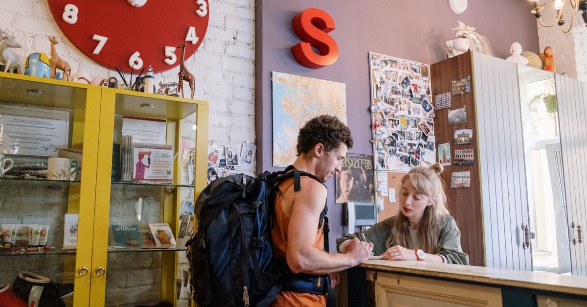 A backpacker at a hostel front desk getting assistance from a receptionist.