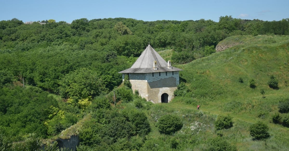 A historic stone building with a pyramid roof in a lush green landscape during a sunny day.