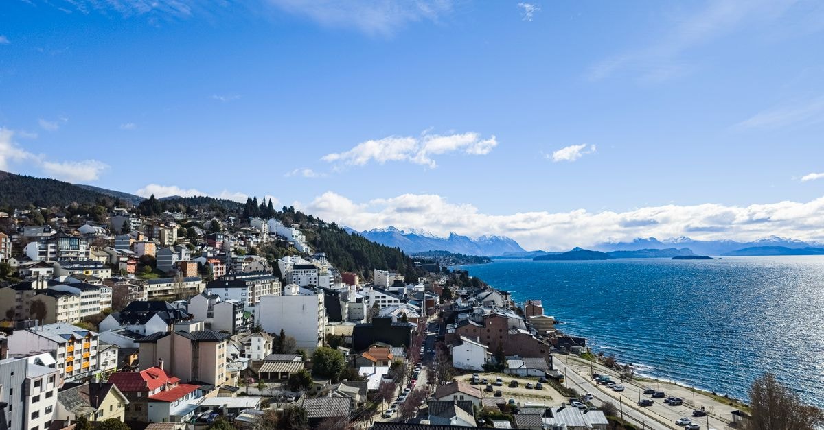 Scenic aerial view of San Carlos de Bariloche with cityscape and lake under a bright blue sky.