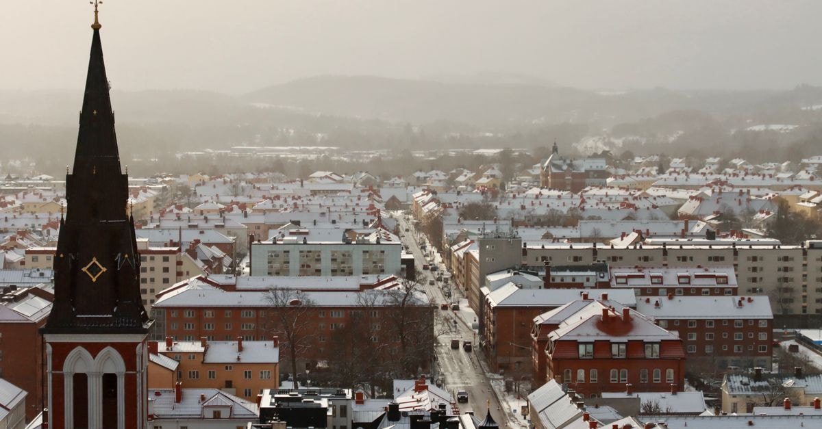 A wintry cityscape featuring a striking bell tower amidst snow-covered buildings under a foggy sky.
