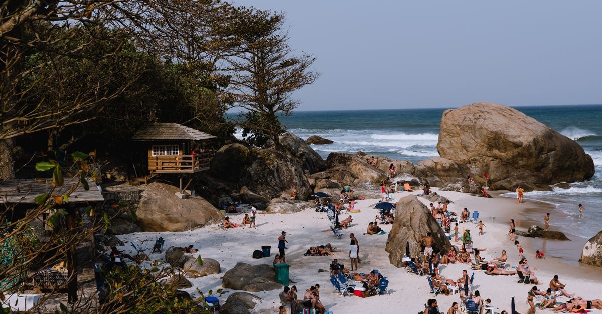 Lively beach in Rio de Janeiro with people enjoying the sun by the rocky shoreline.