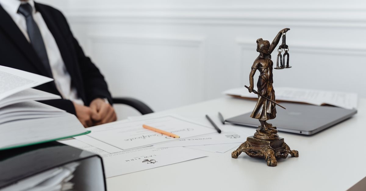 SEC Agrees To Comply With Louisiana Court Order Allowing Ex-NFL Players At LSU A legal professional's workspace featuring Lady Justice statue, documents, and a laptop.