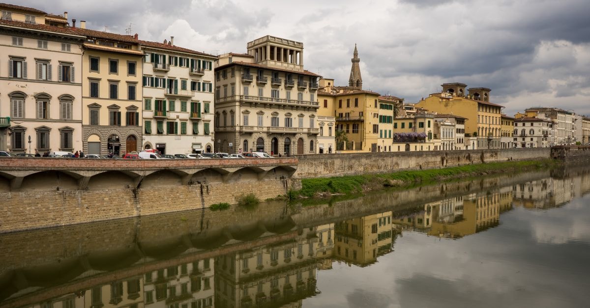 Scenic view of historic buildings reflected in the river in Florence, Italy under cloudy skies.