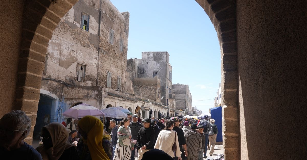 Riad Le Cheval Blanc in Safi: A Rooftop View Over the Old Medina Bustling market scene in Essaouira, Morocco, with people and historical architecture under a bright sky.