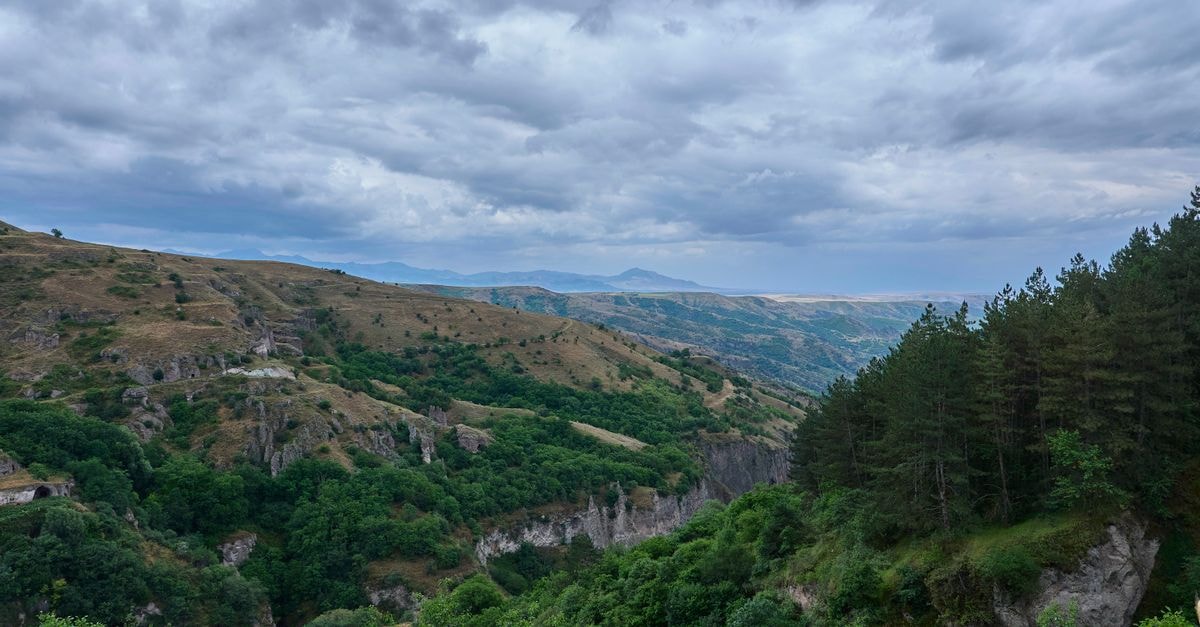 Armenia Travel Guide: Planning Tips, Costs and Things to Do Breathtaking view of Khndzoresk Gorge with lush greenery and rugged hills under a cloudy sky.
